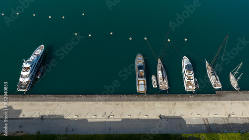 Fototapeta Naklejka Na Ścianę i Meble -  Aerial view of boats anchored at a pier. There is a pedestrian street that runs along the coast.