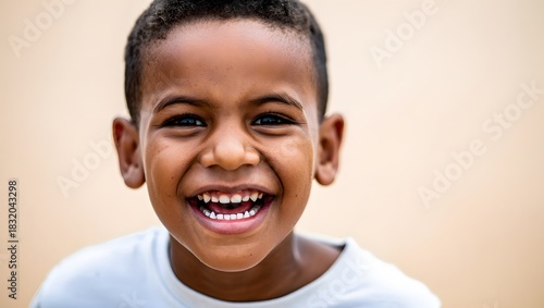 portrait of a laughing 6–7 year old boy wearing a simple T-shirt, standing against a soft light background