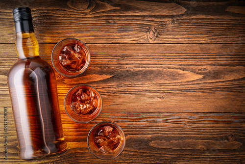 Whiskey Bottle and Glasses with Ice on Wooden Table – Top View