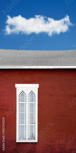 Church window on red brick wall with sloped rough under  white puffy cloud