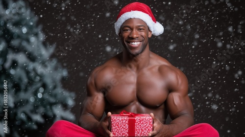 Smiling african male with santa hat holding gift in snowy christmas scene