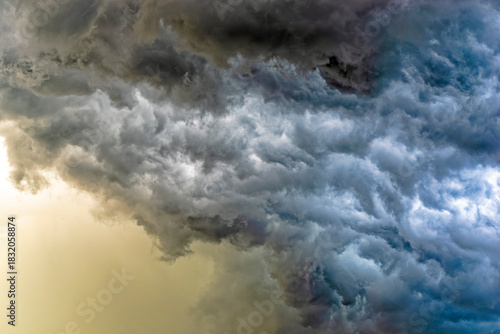 Fotografija detail of intense dark storm clouds lit from behind with glowing yellow sun ligh