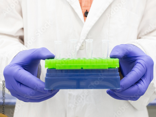 The scientist holds a tripod with small Eppendorf tubes in front of him.