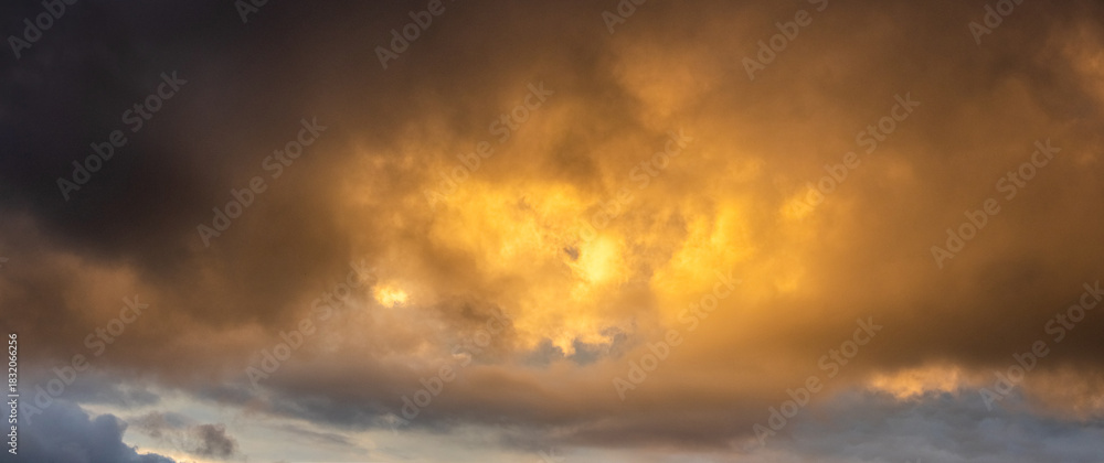 Fototapeta premium Epic panoramic view golden rain clouds during sunset or sunrise breaking through dark storm clouds creating powerful heavenly background with bright light