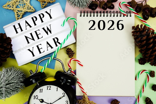 Happy New Year 2026 text with alarm clock and christmas decoration on pastel background