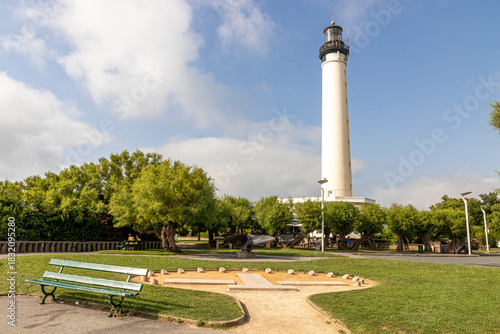Biarritz, France. Full view of the white lighthouse rising above the surrounding garden vegetation under a lightly clouded summer sky