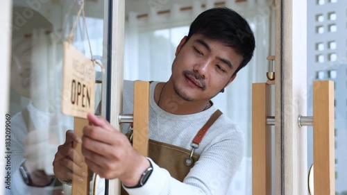 Small business coffee shop owner or employee, cafe entrepreneur preparing to open store, barista man showing open sign with friendly attitude, expressing working spirit, daily task welcoming customers