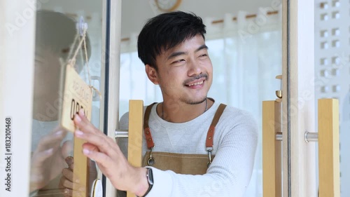 Small business coffee shop owner or employee, cafe entrepreneur preparing to open store, barista man showing open sign with friendly attitude, expressing working spirit, daily task welcoming customers