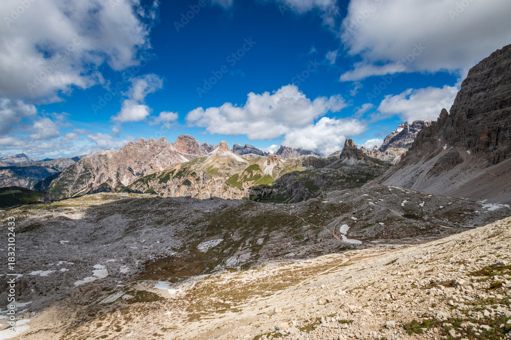 Fototapeta premium Panorama in the Dolomites, Italy with Rautkofel and Monte Paterno at Parco Naturale Tre Cime; pale limestone towers above scree against blue sky with clouds