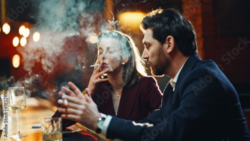 Well-dressed pair enjoying cigarette smoke relaxing at cafe bar counter closeup
