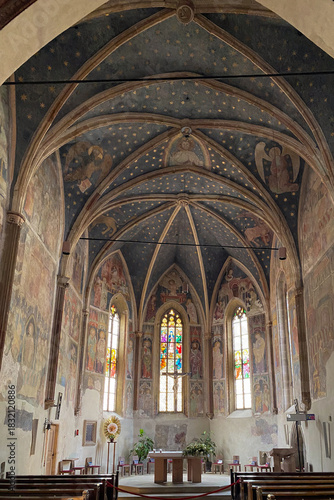 Gothic interior of the Parish Church of the Assumption in Terlan (Terlano), Itayl; rib vault with starry ceiling, fresco cycle and stained glass behind the altar in soft light