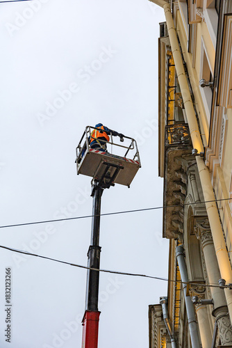 A worker in a raised constriction lift, performing maintenance on a historic building facade. Safety gear, work at height,
