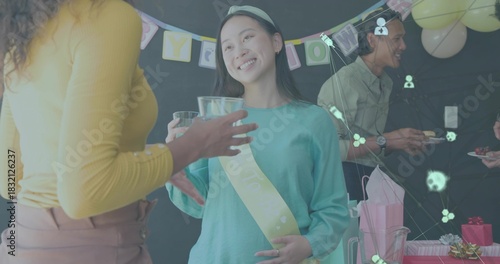 Celebrating woman wearing pale yellow sash and teal top raising clear glass at home with gifts
