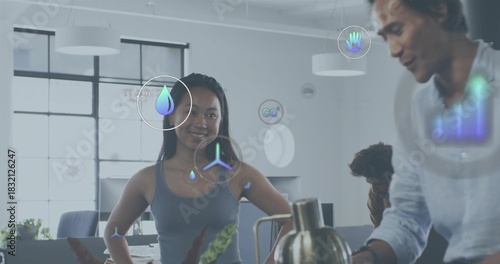 Standing woman in sleeveless grey top guiding team in open-plan office, with kettle and AR icons