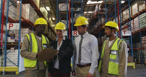 Inspecting team of four checking clipboard in warehouse aisle, wearing hard hats hivis vests jacket