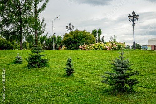 Peaceful Scene With Small Evergreen Trees, Flower Bed, And Classic Lampposts In Victory Park at Poklonnaya Hill, Moscow, Russia, 10 August 2025