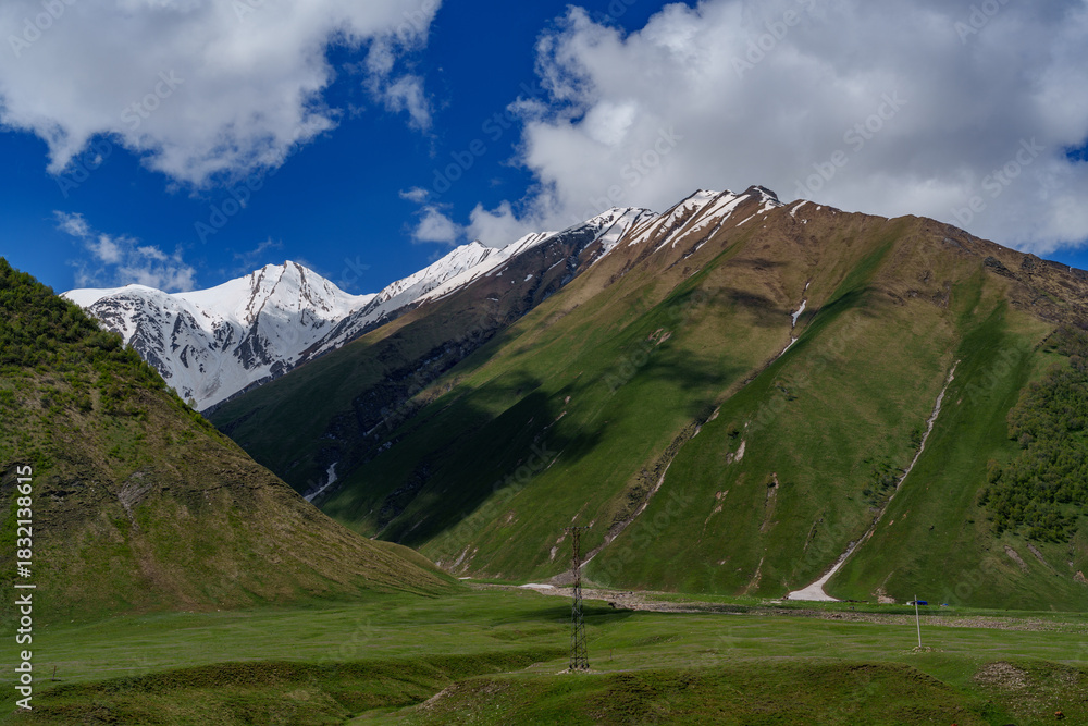 Fototapeta premium Snowy Caucasus ridges above smooth green valley with power masts
