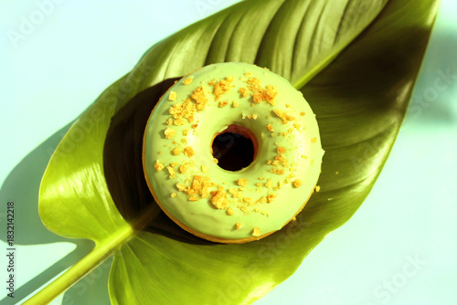 Green Frosted Donut with Crumbs on Tropical Leaf Background