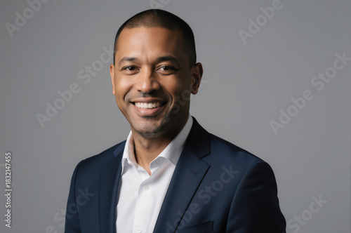 Confident African American businessman presents warm, friendly smile, radiating positivity and approachability. His professional demeanor, dressed sharp dark suit against simple grey background