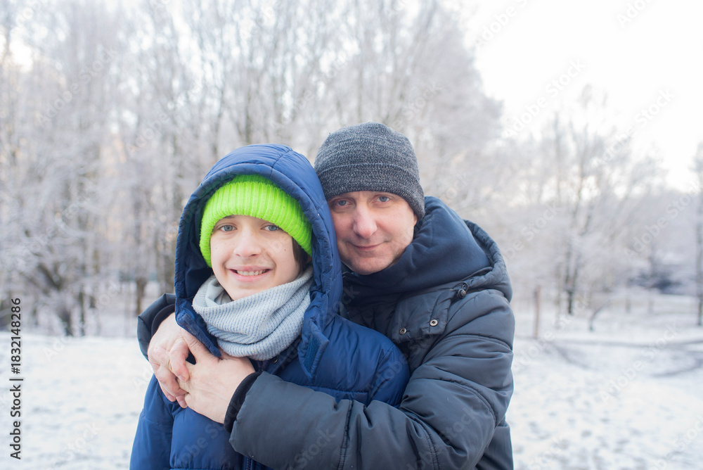 Fototapeta premium A father hugs his teenage son, the boy and his dad pose for a photo in a winter snowy park