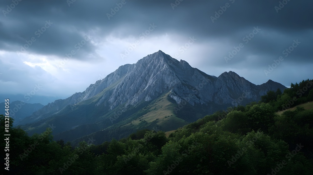 Fototapeta premium Dramatic mountain peak under stormy cloudy skies at dusk with lush green foreground