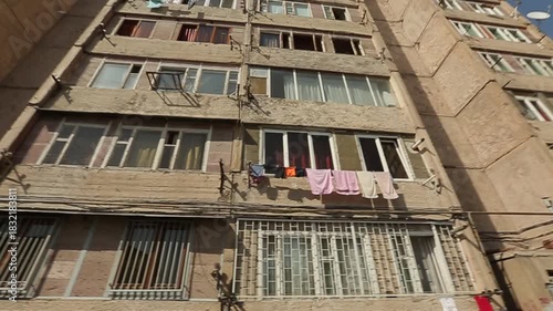 Exterior of weathered multi-story apartment block. Typical socialist architecture with mismatched windows and laundry hanging on balconies. Urban residential scene in a city district.

