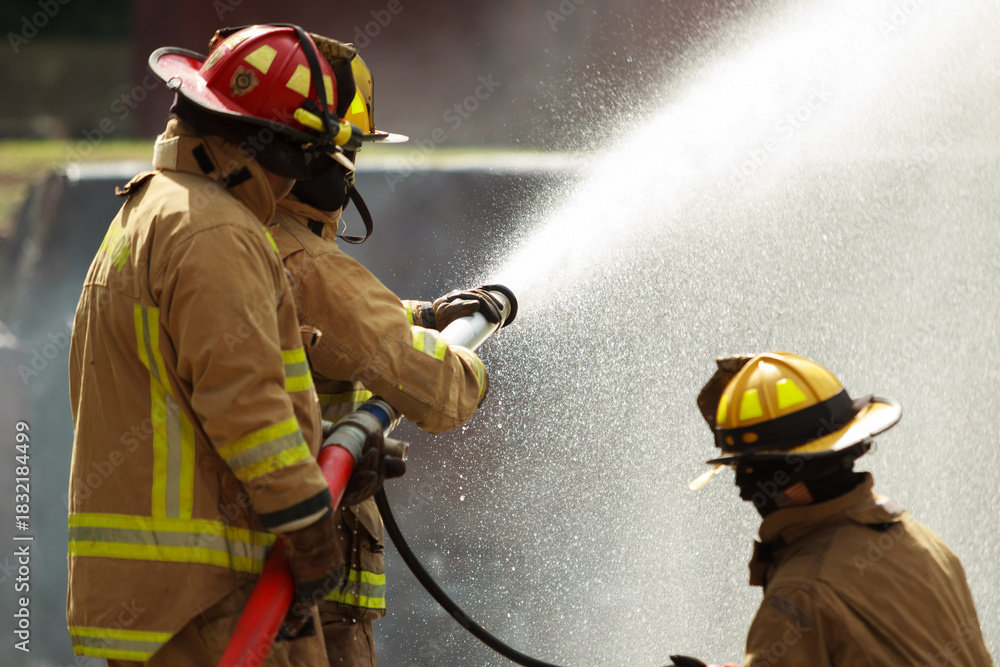 Fototapeta premium Firefighters spraying water to control extinguish an intense blaze.