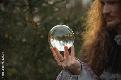 Person holds clear crystal ball while standing amidst trees in autumn light
