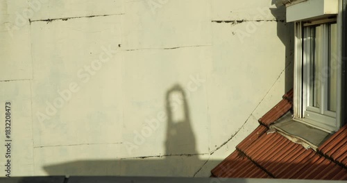 A man's shadow is cast on the wall of a building, arriving and beginning to stretch out under the warm, orange light of dawn in the city.