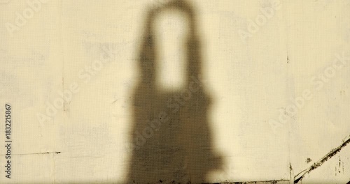 A man's shadow cast on the wall of a building as he stretches his arms and moves his body from side to side under the orange light of dawn in the city. 