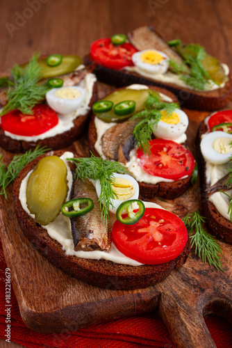 open sandwiches with sprats, vegetables and herbs, on a wooden board, breakfast, snack,