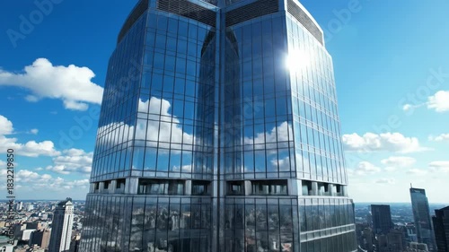 Modern glass skyscraper reflecting sunlight and clouds in urban landscape