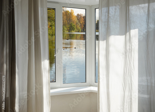 View from the window  on autumn landscape with a lake and bright yellow trees on the river bank.