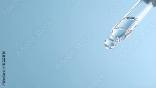 Clear dropper dripping liquid on blue background. Science, medicine, or cosmetic product concept.