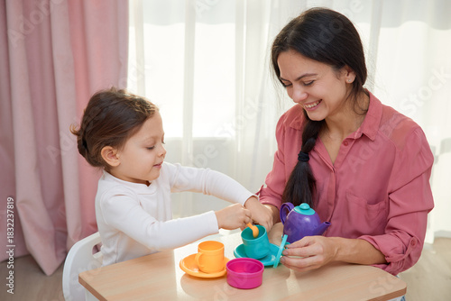 Mother and daughter enjoying a pretend tea party with colorful toy dishes