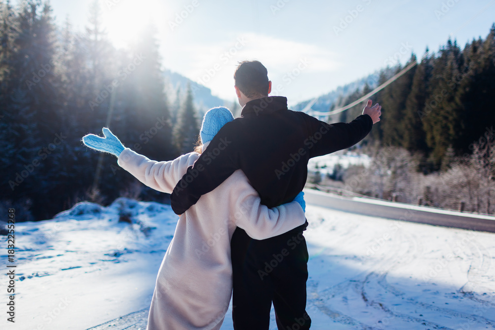 Obraz premium Back view of happy couple in love hugging on background of winter Carpathian mountains by car. Travelling by auto