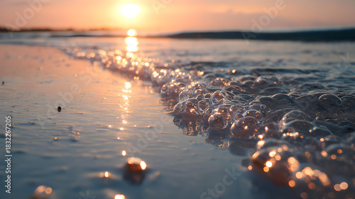Fototapeta Naklejka Na Ścianę i Meble -  Gentle ocean wave washes over sandy shore at sunset, creating a peaceful, shimmering scene.