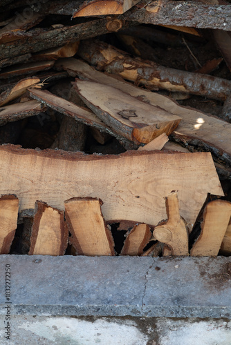 Vertical image of stacked firewood placed against a concrete base.