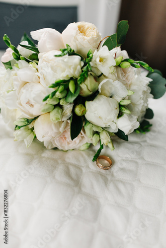 Close-up of wedding rings placed on a bouquet of white flowers. Soft natural light highlights the delicate petals, greenery, and golden bands, creating a romantic and elegant wedding detail shot.