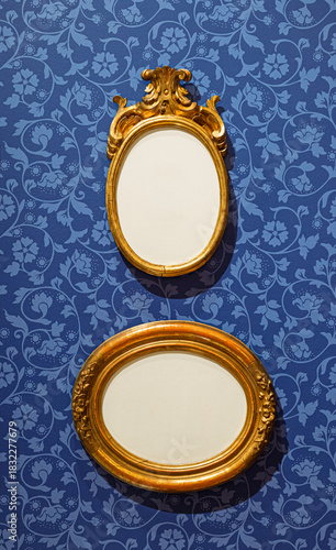 Wallpaper Mural Two antique oval gold frames hanging on a blue wall with floral damask wallpaper. Ornate empty photo frames with copy space for art. Torontodigital.ca