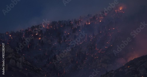 Burning and smoking rocky mountain side at dusk