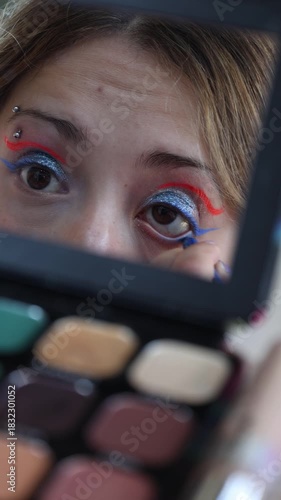 A Caucasian girl applying blue eyeliner to her lower eyelid, vertical shot in slow motion.