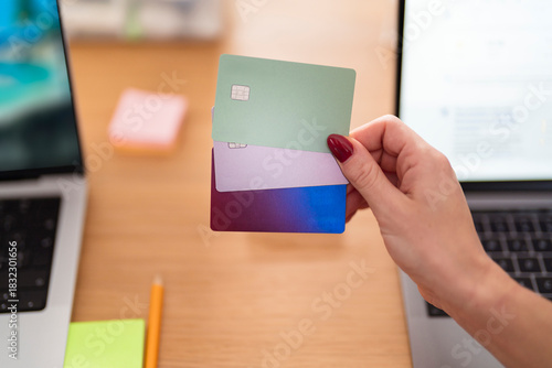 A person holds three credit cards, one green, one purple, and one blue, in front of a laptop, symbolizing financial management and online transactions.