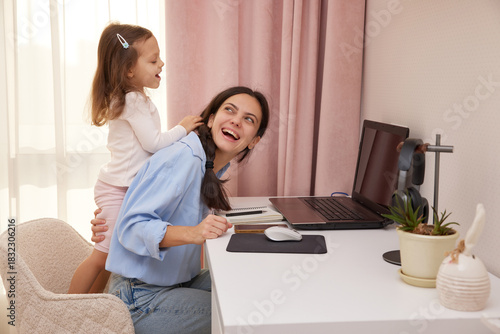 Happy mother working from home laughing while child plays and distracts her