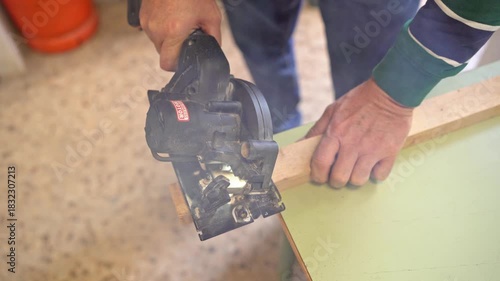 Close-up of craftsman hands cutting a long wooden board with a cordless circular saw in the workshop