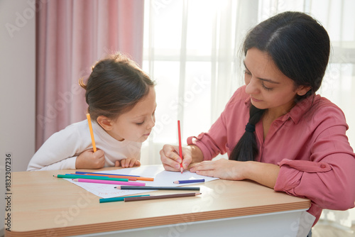 Mother and cute little daughter drawing with colored pencils, engaging in creative home learning