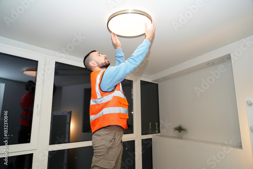 Slika na platnu A Worker specialist is working on installing a new ceiling light fixture in the living room