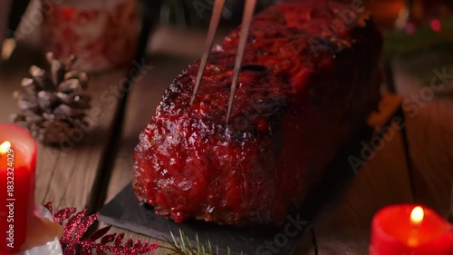 Slicing homemade meatloaf with tomato glaze. Juicy meat on a festive Christmas table with candles and decorations. Traditional holiday dinner main course