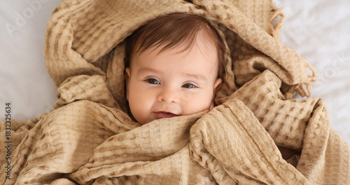 Cute little baby with beige plaid lying on bed, closeup