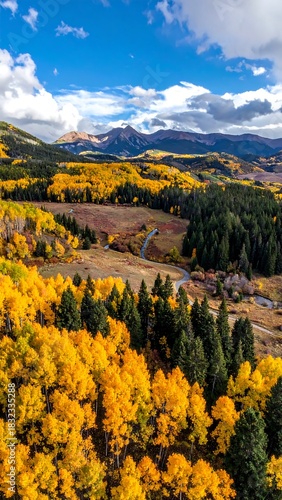 Aerial view of a valley during autumn with golden foliage, a winding stream, and mountains against a bright blue sky